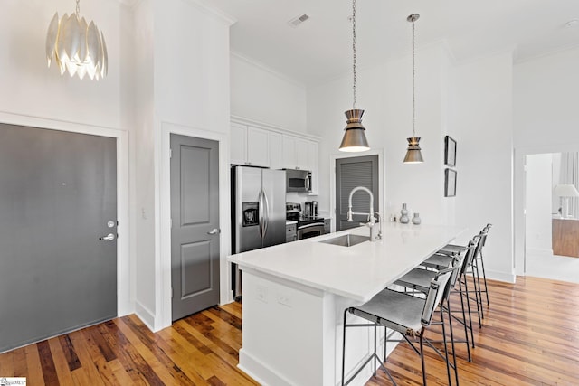 kitchen featuring hanging light fixtures, white cabinetry, appliances with stainless steel finishes, a breakfast bar area, and sink