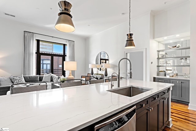 kitchen featuring light stone counters, stainless steel dishwasher, pendant lighting, light wood-type flooring, and sink