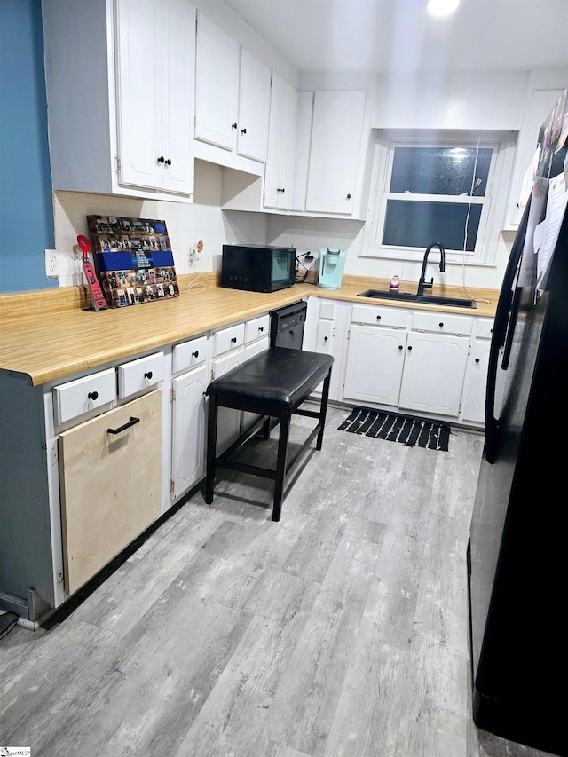 kitchen with black appliances, light hardwood / wood-style flooring, white cabinetry, and sink