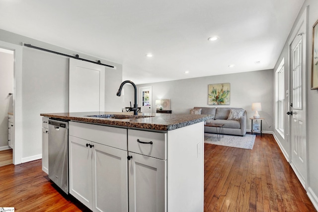 kitchen featuring stainless steel dishwasher, an island with sink, a barn door, white cabinetry, and sink