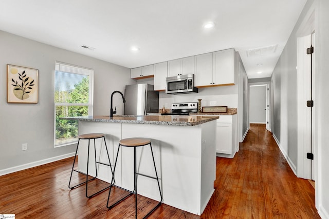 kitchen with stainless steel appliances, white cabinetry, hardwood / wood-style flooring, stone countertops, and a kitchen island with sink