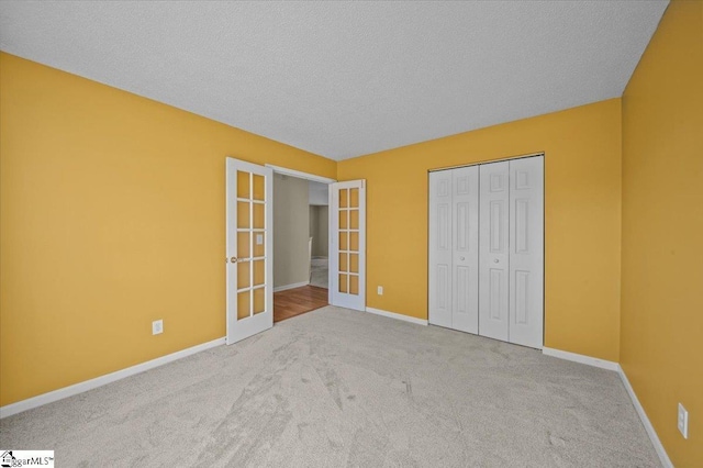 unfurnished bedroom with a textured ceiling, french doors, a closet, and light carpet