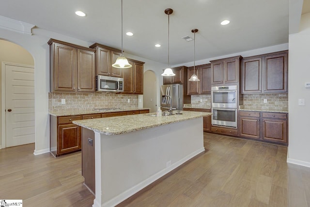 kitchen with appliances with stainless steel finishes, hanging light fixtures, a kitchen island with sink, and light stone countertops