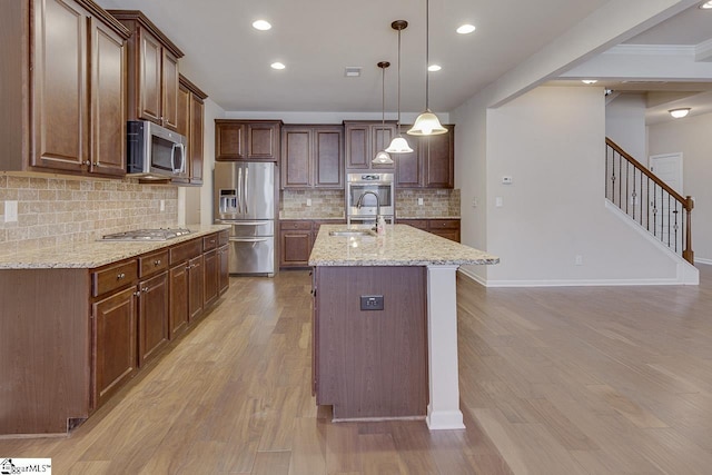 kitchen featuring a center island with sink, appliances with stainless steel finishes, pendant lighting, light stone counters, and sink