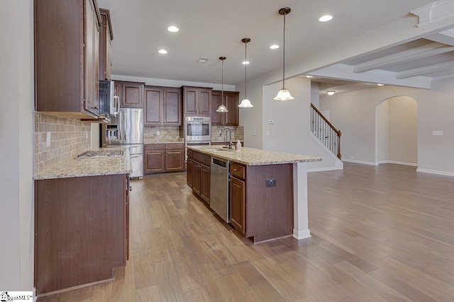 kitchen with a center island with sink, appliances with stainless steel finishes, pendant lighting, beam ceiling, and sink