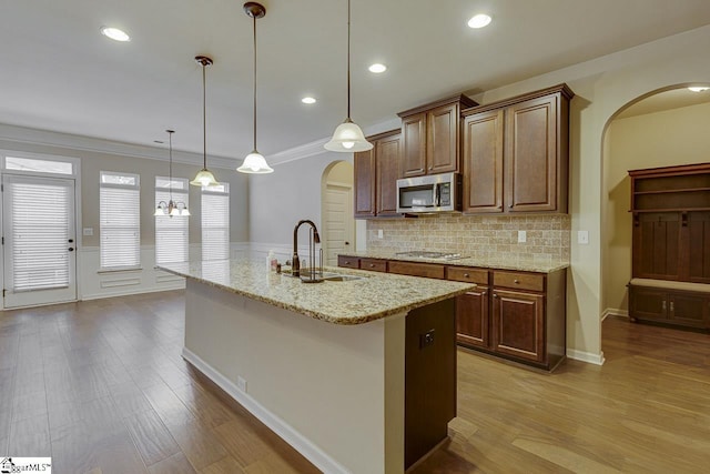 kitchen featuring a kitchen island with sink, appliances with stainless steel finishes, pendant lighting, light stone counters, and sink