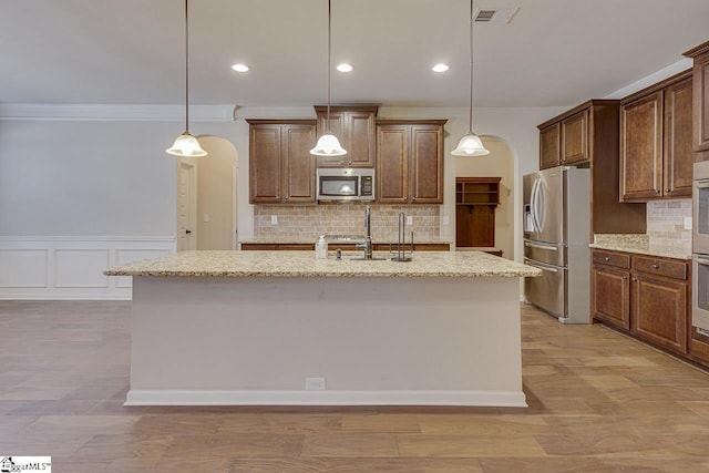 kitchen featuring stainless steel appliances, a center island with sink, and decorative light fixtures