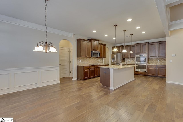 kitchen with ornamental molding, an island with sink, backsplash, hanging light fixtures, and appliances with stainless steel finishes