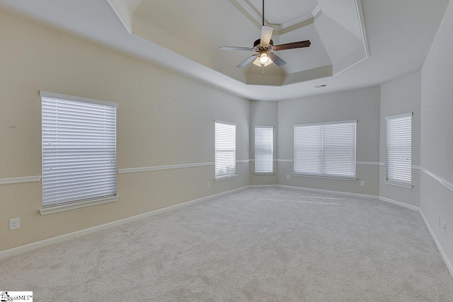 empty room featuring ceiling fan, light colored carpet, and a raised ceiling