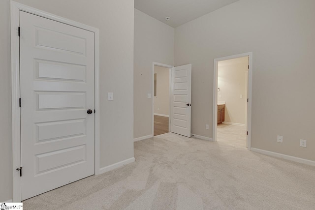 unfurnished bedroom featuring a high ceiling, light carpet, and connected bathroom