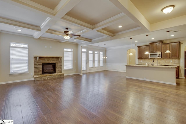 unfurnished living room with coffered ceiling, a stone fireplace, ceiling fan, ornamental molding, and beam ceiling