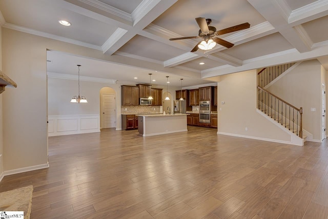 unfurnished living room featuring beam ceiling, ceiling fan with notable chandelier, ornamental molding, coffered ceiling, and sink