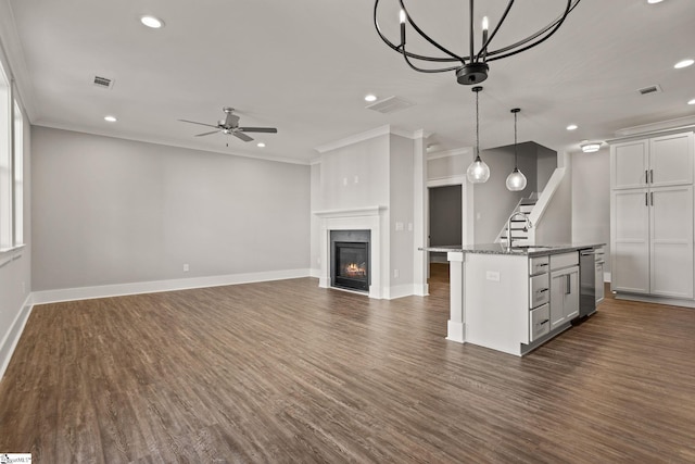 kitchen featuring dark stone counters, a center island with sink, crown molding, and hanging light fixtures