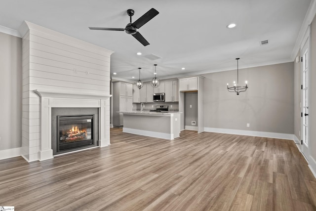 unfurnished living room featuring ceiling fan with notable chandelier, ornamental molding, and light wood-type flooring