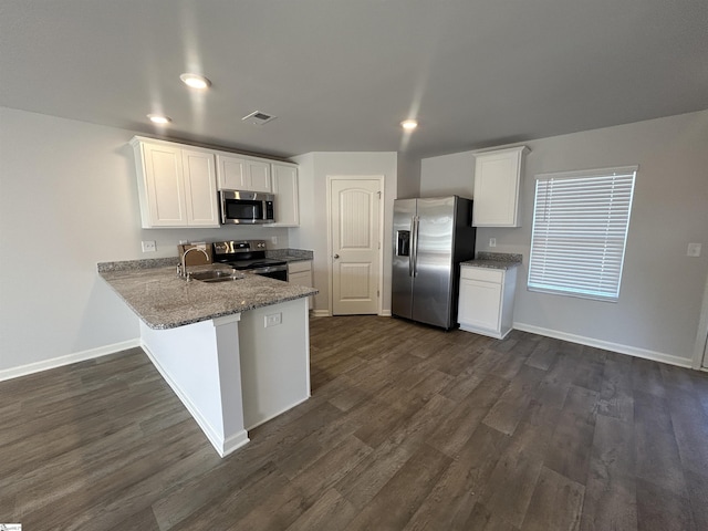 kitchen with appliances with stainless steel finishes, kitchen peninsula, dark wood-type flooring, sink, and white cabinetry