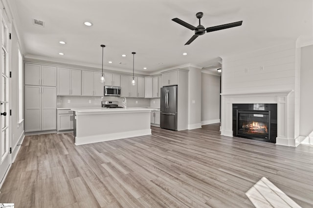 kitchen with a center island with sink, stainless steel appliances, crown molding, pendant lighting, and decorative backsplash