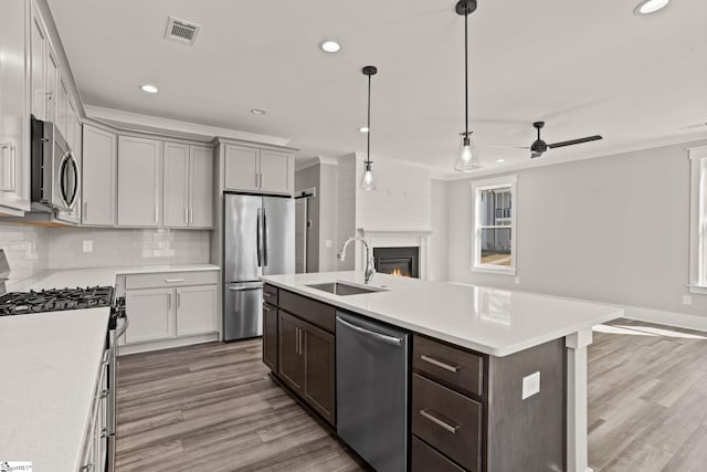 kitchen with stainless steel appliances, sink, ceiling fan, a large fireplace, and an island with sink