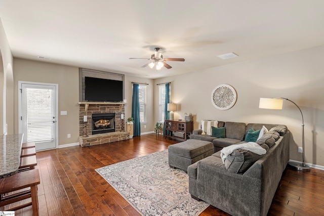 living room with ceiling fan, dark wood-type flooring, and a stone fireplace