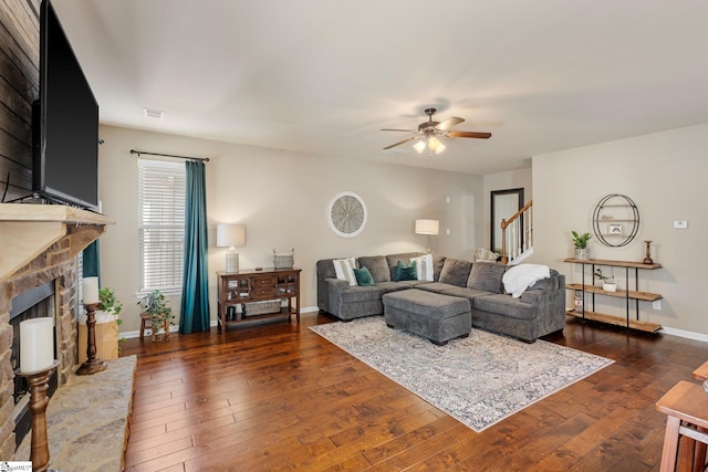 living room featuring ceiling fan, dark hardwood / wood-style flooring, and a stone fireplace