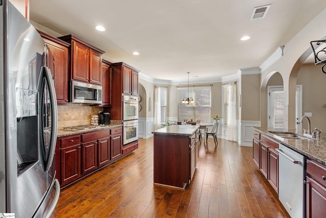 kitchen with pendant lighting, stainless steel appliances, a kitchen island with sink, dark stone counters, and sink