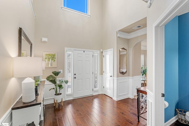 foyer entrance featuring a towering ceiling, crown molding, and dark wood-type flooring