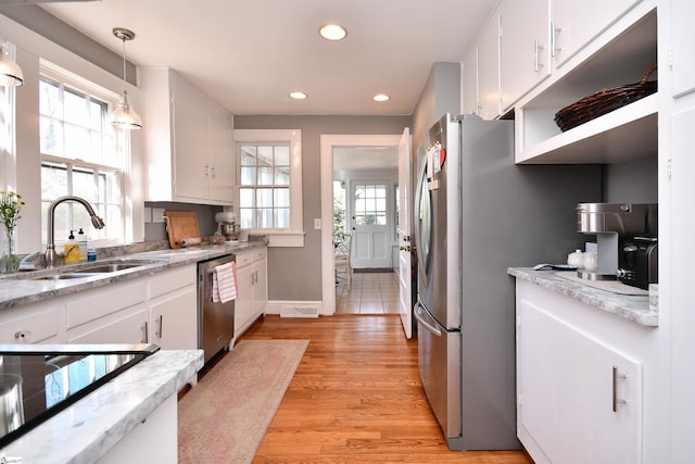 kitchen with white cabinets, appliances with stainless steel finishes, pendant lighting, sink, and light hardwood / wood-style flooring