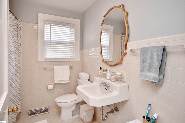 bathroom featuring toilet, tile patterned flooring, tile walls, and sink