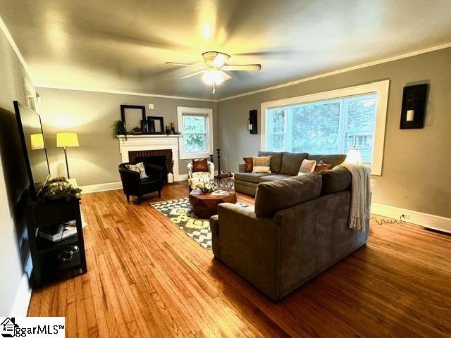 living room with hardwood / wood-style floors, a brick fireplace, ceiling fan, and ornamental molding