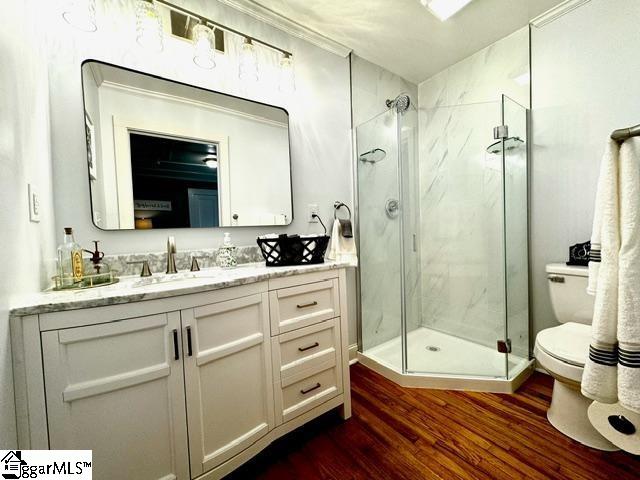 bathroom with toilet, wood-type flooring, vanity, and a shower with shower door