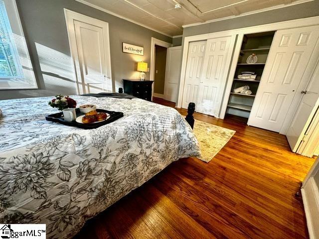 bedroom with two closets, ornamental molding, and hardwood / wood-style floors