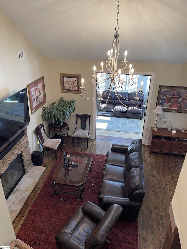 living room featuring dark hardwood / wood-style flooring, a chandelier, and a stone fireplace