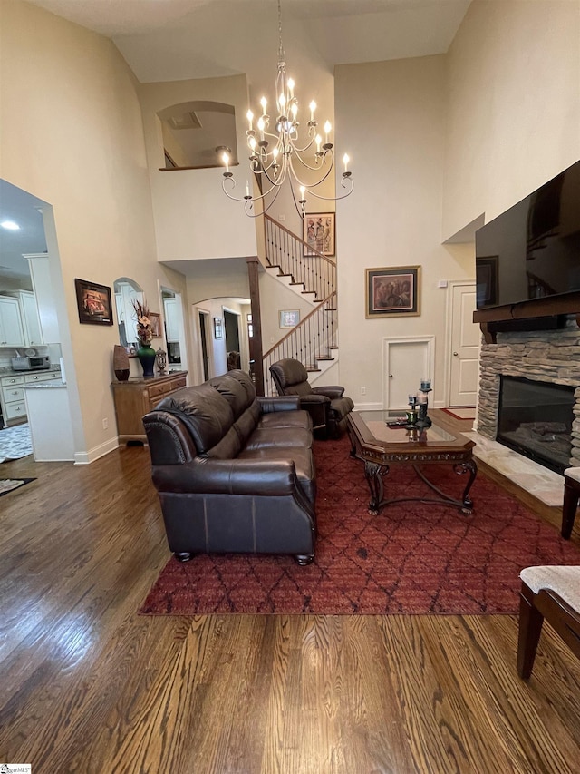 living room with wood-type flooring, a high ceiling, an inviting chandelier, and a stone fireplace