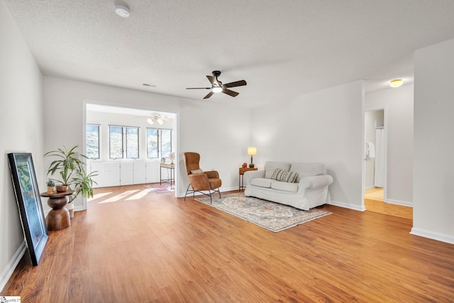 living room featuring ceiling fan, light wood-type flooring, and a textured ceiling