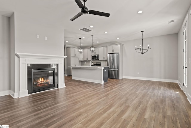 unfurnished living room with ceiling fan with notable chandelier, sink, and hardwood / wood-style flooring