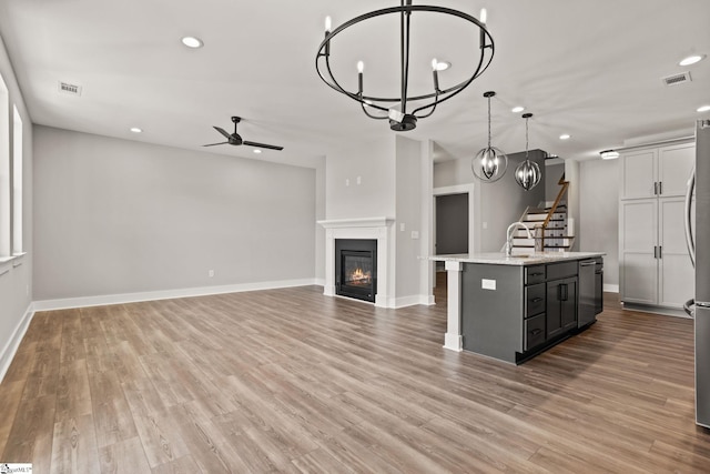 kitchen featuring light stone counters, light hardwood / wood-style flooring, ceiling fan with notable chandelier, hanging light fixtures, and a kitchen island with sink