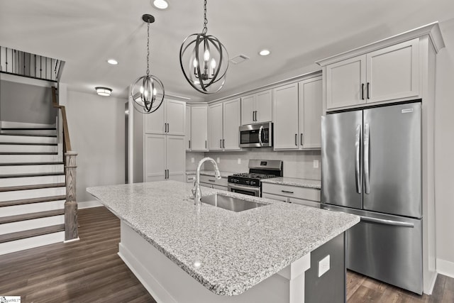 kitchen with sink, decorative light fixtures, an island with sink, light stone countertops, and appliances with stainless steel finishes