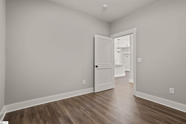 spare room with a notable chandelier and dark hardwood / wood-style floors