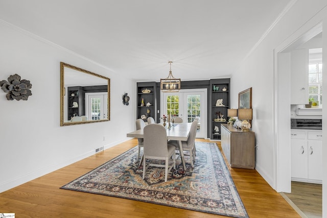 dining room featuring a notable chandelier, light hardwood / wood-style flooring, french doors, and built in features