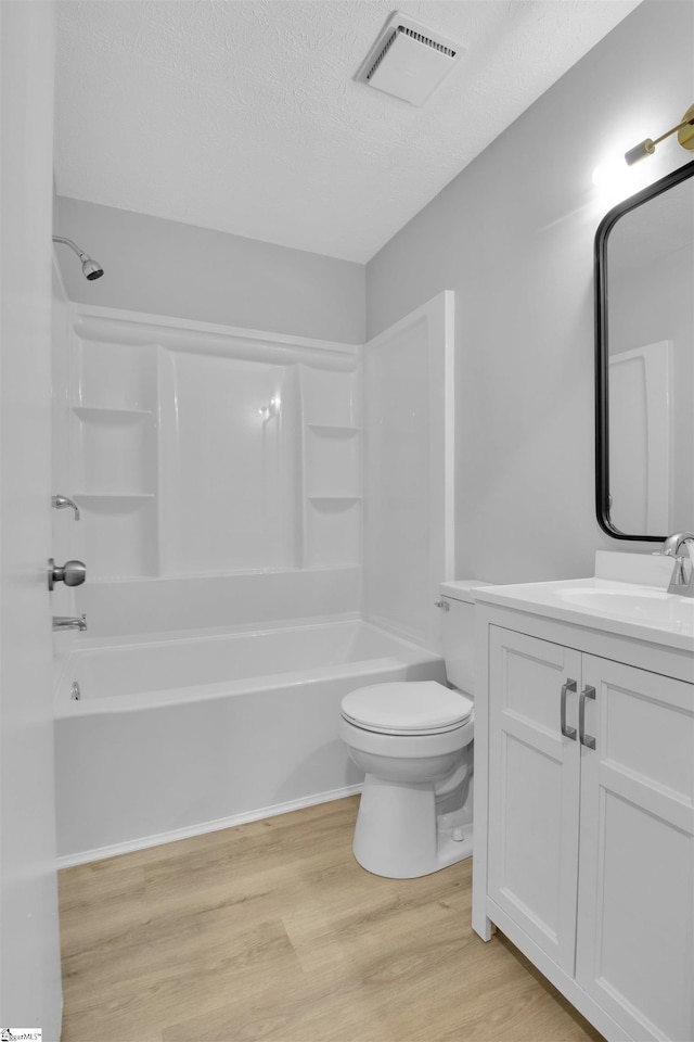 full bathroom with toilet, wood-type flooring, vanity, a textured ceiling, and shower / bathing tub combination