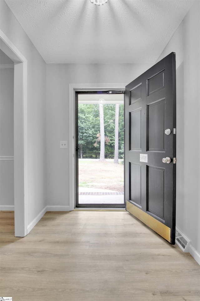 doorway to outside featuring light wood-type flooring and a textured ceiling