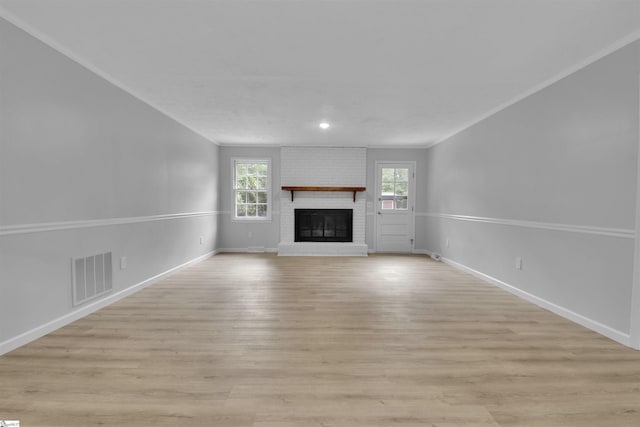 unfurnished living room featuring ornamental molding, light wood-type flooring, and a brick fireplace