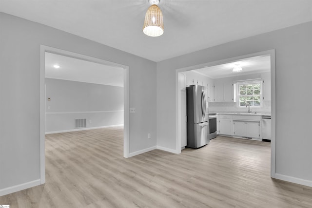 kitchen featuring stainless steel appliances, light wood-type flooring, sink, white cabinetry, and tasteful backsplash