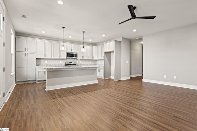 kitchen featuring dark hardwood / wood-style floors, decorative light fixtures, stainless steel appliances, a center island with sink, and ceiling fan