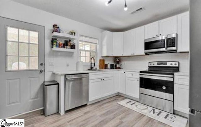 kitchen featuring sink, white cabinets, light wood-type flooring, decorative backsplash, and appliances with stainless steel finishes