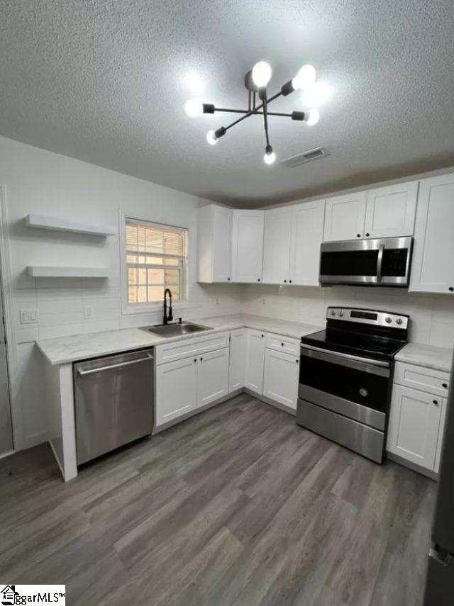 kitchen with a textured ceiling, appliances with stainless steel finishes, white cabinetry, and sink