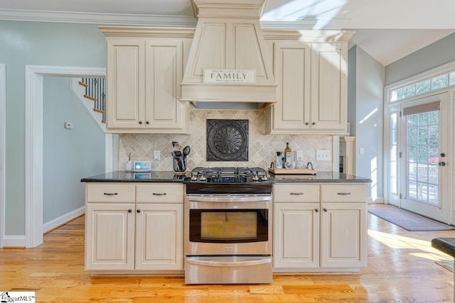 kitchen with light hardwood / wood-style floors, stainless steel range with gas stovetop, tasteful backsplash, and custom range hood