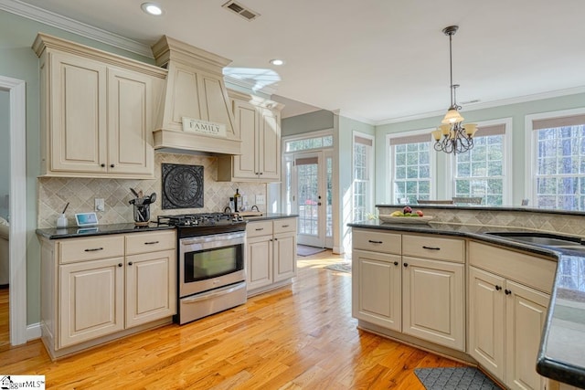 kitchen with decorative light fixtures, cream cabinetry, french doors, stainless steel gas range oven, and premium range hood