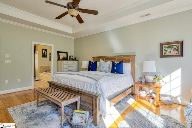 bedroom with a raised ceiling, ensuite bath, light wood-type flooring, ceiling fan, and ornamental molding