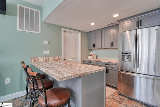 kitchen featuring a breakfast bar area, gray cabinetry, stainless steel fridge, butcher block countertops, and a kitchen island