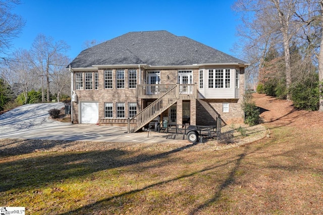 rear view of property featuring a garage, a wooden deck, a yard, and a patio area